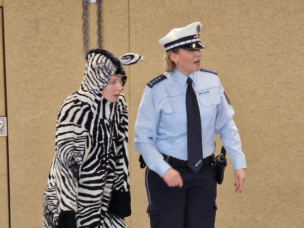 Die Polizistin hilft dem Zebra über die Straße.